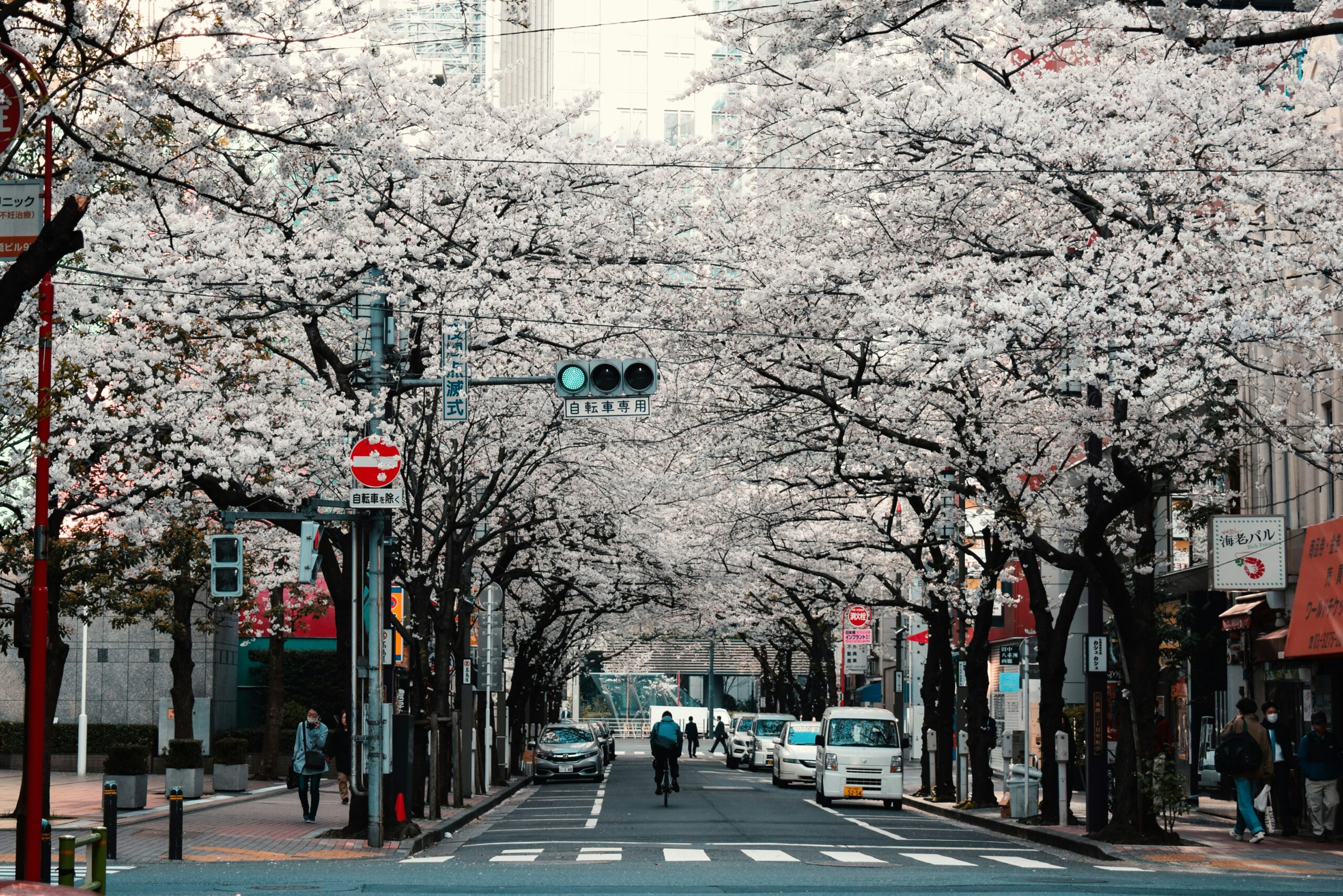Une rue japonaise animée, entourée d'arbres, où des piétons se déplacent