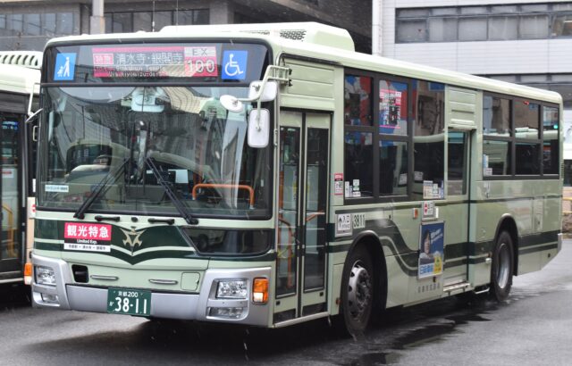 Bus express touristique EX100 du réseau municipal de Kyoto, vert et crème, affichant les destinations Kiyomizu-dera et Ginkaku-ji, à l'arrêt devant la gare de Kyoto sous la pluie.